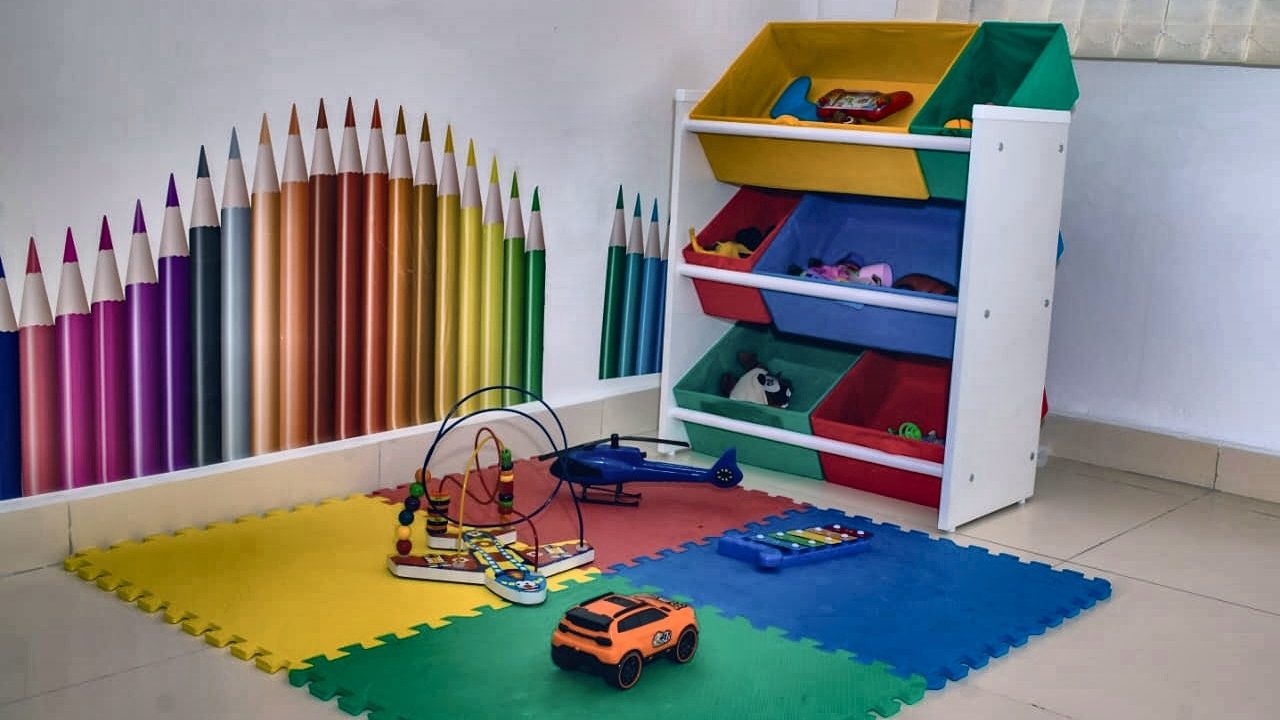 Sala de atendimento infantil do Núcleo Ser Plural, com parede decorada por lápis de cor, tapete de encaixe e organizador de brinquedos